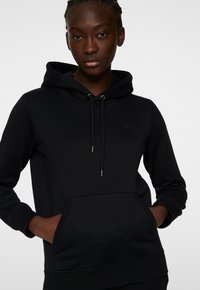 Svart hoodie gjord av mjukt tyg. Har en känguruficka, justerbar dragsko och ribbade muddar och fåll. Diskret logotypdetalj.