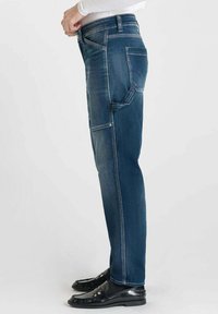 Jeans slim fit bleus avec un design classique à cinq poches, fabriqués en denim. Présentent des coutures contrastées et une coupe droite.