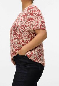 Top de manga corta con patrón rojo y crema, de corte holgado y escote redondeado, combinado con jeans de mezclilla oscuros, que presenta un bolsillo lateral.