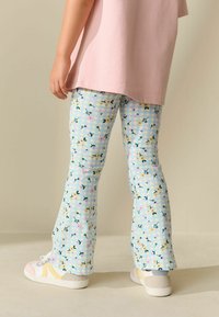 Pantaloni a zampa di elefante azzurri con motivo floreale in giallo, rosa e verde, abbinati a una maglietta rosa e sneakers bianche.