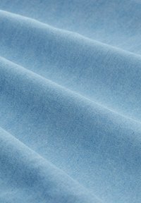 Zacht lichtblauw stof met zachte plooien die textuur en weefpatroon tonen in close-up.