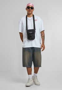 Black crossbody bag, white oversized t-shirt, faded blue denim shorts, pink bandana, sunglasses, white sneakers, and silver chain necklace.