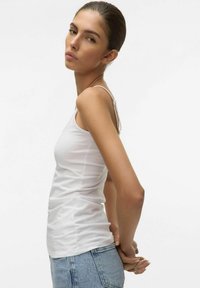 Top bianco fitted in cotone elastico, con spalline sottili e una texture morbida, abbinato a pantaloni corti in denim a vita alta.