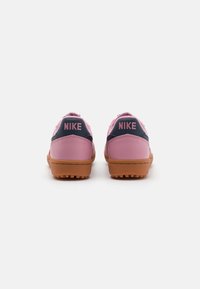 Rosa lær-sneakers med marineblå detaljer, flat gummisåle og "NIKE" merke på hælen. Har en lavskåret design og polstret krage.