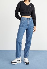 Svart kortärmad huvtröja med V-urringning och Nike-logga, tillsammans med högmidjade blå denimjeans och vita och svarta sneakers.