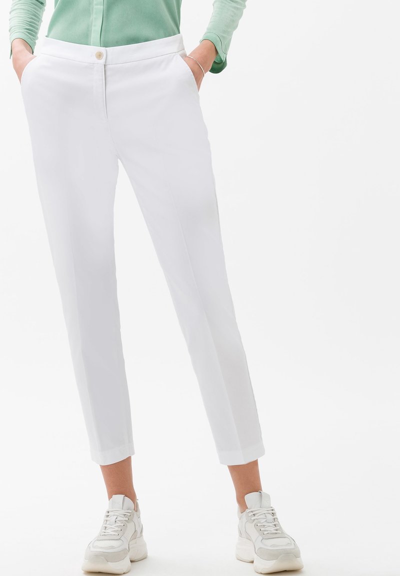 Pantaloni bianchi su misura con vita aderente, tasche laterali e chiusura a un bottone. Indossati con sneaker bianche. Tessuto morbido.