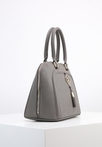 Borsa a tracolla in pelle grigia con forma strutturata, doppi manici, hardware dorato, zip laterale e un accento a frange. Texture liscia, design angolare.