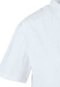 White short-sleeve shirt featuring a pointed collar, smooth cotton material, and side slits at the hem for ease of movement.