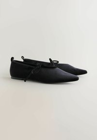 Pantofi negri cu talpă plată, cu un design cu vârf ascuțit, realizați dintr-un material moale. Acestia au un stil minimalist, cu un detaliu mic sub formă de fundiță în față.