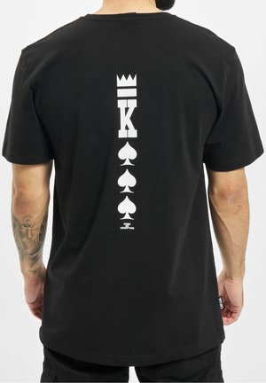 Sort bomuld t-shirt med et centralt vertikalt design af en krone, et "K" og tre kløftesymboler i hvid på ryggen.