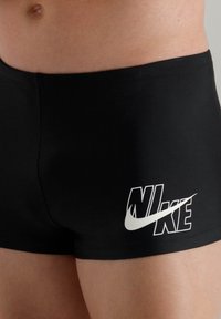 Shorts de sport noirs en matériau extensible, avec un logo Nike blanc sur la jambe gauche et un design ajusté pour une utilisation active.