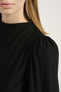 Black fabric garment with a high neckline and puffed sleeve detail. Smooth texture, minimalistic design focusing on silhouette.