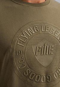 Olijfgroene katoenen sweatshirt met een reliëf cirkelvormig logo met tekst en schilddesign; zachte textuur en geribde halslijn.