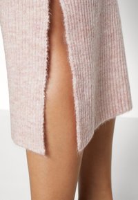 Närbild av en räfflad rosa ullkjol med en framfåra som visar bar hud mot en ljus bakgrund.