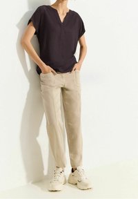 Haut violet foncé à manches courtes avec un col en V, associé à un pantalon beige clair et des baskets blanches. Design simple et épuré avec des poches.