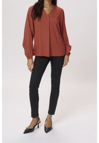 Rustfarvet bluse med tekstureret mønster og V-hals, parret med sorte slim-fit bukser og sorte lakerede slingback hæle.