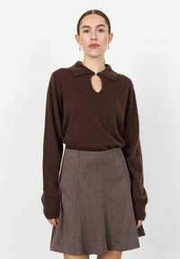 Suéter de punto marrón con un escote en forma de ojal y un cuello, combinado con una falda gris acampanada que presenta un patrón sutil y un acabado texturizado.