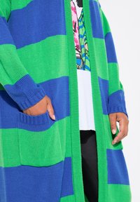 Cardigan a righe verdi e blu con vestibilità rilassata, polsini a costine e tasche. Materiale in maglia leggero, design aperto davanti.
