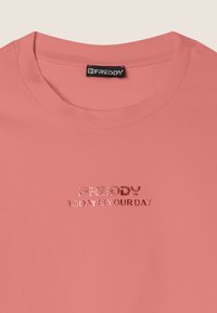 T-shirt di cotone rosa con colletto rotondo, maniche corte e testo metallico argento, "FREDDY OGGI È IL TUO GIORNO," centrato sulla parte anteriore.