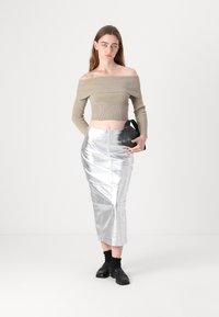 Beige ribbed crop top yang off-the-shoulder dipasangkan dengan rok midi metalik perak, yang memiliki potongan ramping dan kilau halus, dilengkapi dengan aksesori hitam.
