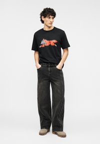 Μαύρο βαμβακερό T-shirt με κόκκινο καρτουνίστικο σχέδιο στο μπροστινό μέρος, συνδυασμένο με φαρδιά μαύρα τζιν με ραφές στο πλάι.