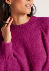 Flauschiger magentafarbener Pullover mit einem gerippten Rundhalsausschnitt und lockerer Passform. Verfügt über ein strukturiertes Strickmuster und eine weiche Optik. Enthält einen Ring mit floralem Design.