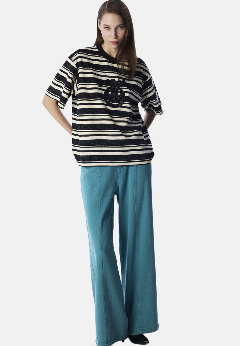 Camisa de manga corta a rayas blancas y negras con un diseño de lentejuelas negras, combinada con pantalones de pierna ancha en tela de mezclilla color teal.