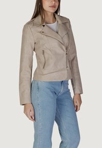 Giacca in ecopelle beige con design corto, zip asimmetrica e due tasche con zip. Caratterizzata da un colletto classico e una superficie liscia.