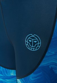 Námořnická modrá neoprenová tkanina s texturovaným modrým vzorem, s světle modrým emblémem na stehně a kontrastním šitím.