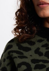 Groene trui met een zwart leopardprintpatroon, gemaakt van zacht breimateriaal met een geribbelde zwarte kraag.