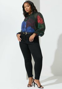 Blusa con stampa floreale in tonalità scure con maniche volant, abbinata a jeans neri aderenti e tacchi alti neri con cinturini. Accentata da una cintura dorata.