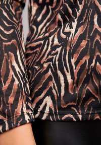 Zebra-mønsteret stoff i varme brune og svarte farger, med en myk, teksturert følelse og synlig søm, samt en avslappet passform ved kanten.