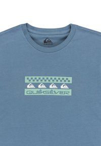 Niebieska koszulka bawełniana z graficznym wzorem z zielonymi akcentami, w kratkę oraz z logo Quiksilver na środku.