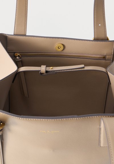 Εσωτερικό μπεζ τσάντας tote με τσέπη με φερμουάρ, ρυθμιζόμενο λουρί και κούμπωμα με μαγνήτη, που δείχνει λείο δέρμα και λεπτομέρειες από χρυσό μέταλλο.
