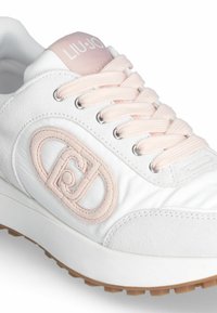 Zapatilla blanca con acentos rosas, con una parte superior de malla texturada, bordado del logo, cordones redondos y una suela de goma con un dibujo texturado.