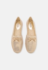 Beige espadrilles gemaakt van gebroken textiel met een gevlochten juten zool, voorzien van een decoratieve strik en logo-gegraveerde metalen accenten.