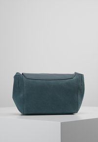 Rektangulär teal-väsk med en mjuk mocka-liknande textur, som har en platt topplock och sydda detaljer i kanterna.