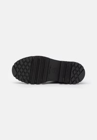 Semelle de chaussure noire avec motif de bande de roulement texturé, comprenant des formes en losange et des rainures horizontales, sur un fond blanc uni.