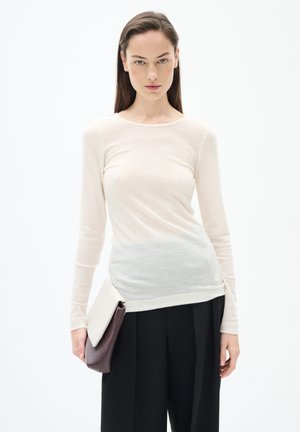 Maglietta leggera a maniche lunghe di colore crema, che sfuma in un grigio chiaro nella parte inferiore. Abbinata a una borsa a due toni e pantaloni neri.