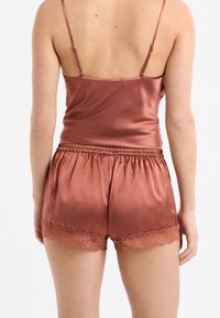 Satin-Top und Shorts-Set in Rostfarbe, mit verstellbaren Trägern, elastischem Bund und Spitzenbesatz an den Shorts.