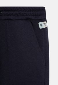 Dunkelblaue Sweatpants aus strukturiertem Material, mit seitlichen Taschen und einem Markenetikett von "Water Dreams". Elastischer Bund sorgt für Komfort.