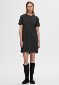 Robe en coton à manches courtes, de couleur gris foncé, avec un col rond et une silhouette droite, arrivant à mi-cuisse. Portée avec des bottes noires jusqu'au genou.