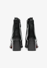 Stivali ankle in pelle nera con punta arrotondata, tacco a blocco e una cerniera discreta sul retro per una facile indossabilità. Texture liscia con dettagli minimi.