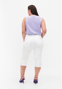 Pantalones capri blancos y una blusa sin mangas color lavanda. Los pantalones tienen bolsillos traseros; la blusa tiene un cuello redondo y una textura suave. Tacones altos morados.