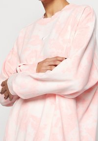 Sudadera de tie-dye rosa con mangas largas, cuello de tripulación y un pequeño logo blanco en el pecho, hecha de una tela suave.