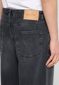 Ciemnoszare dżinsy z denimu z skórzaną naszywką oznaczoną "ONLY & SONS", z dwoma tylnymi kieszeniami i z efektem przetarcia.