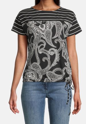 Haut noir à manches courtes avec motifs paisley et floraux blancs, rayures horizontales sur les manches et l'encolure, associé à un jean bleu.