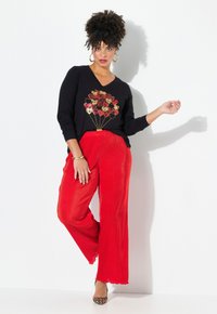 Zwart shirt met lange mouwen, voorzien van een gouden en rode bloem ballontje graphic, gecombineerd met gestructureerde wijde rode broek en dierenprint hakken.