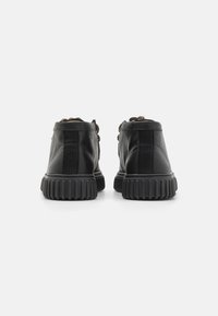 Chaussures en cuir noir avec une finition texturée, présentant une semelle cannelée et des lacets foncés. Design à hauteur de cheville avec des panneaux latéraux élastiques.
