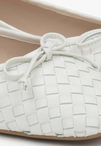 Białe skórzane baletki z plecionym wzorem. Posiadają okrągły czubek i cienki detal w postaci kokardki na wierzchu. Gładkie wykończenie wnętrza.